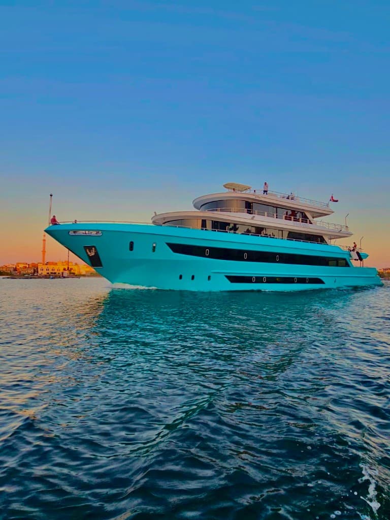 SARAH & MO 2 cruising the Red Sea at golden hour, her turquoise hull mirrored in calm water.